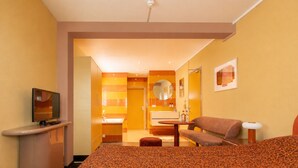 A hotel room with a bed, a TV, a sofa, a small table, and a bathroom visible through an open door. - Domburg4you (Domburg)