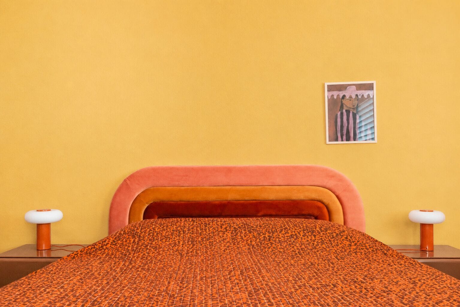 Ein Bett mit einer gemusterten Decke, einem pinken Kopfteil und einem gerahmten Bild an der Wand.