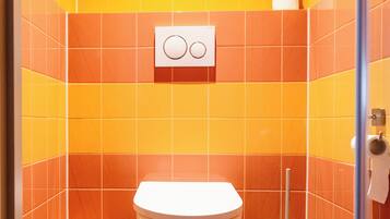 A bathroom with orange tiles, a white toilet, a trash bin, and a paper towel dispenser.