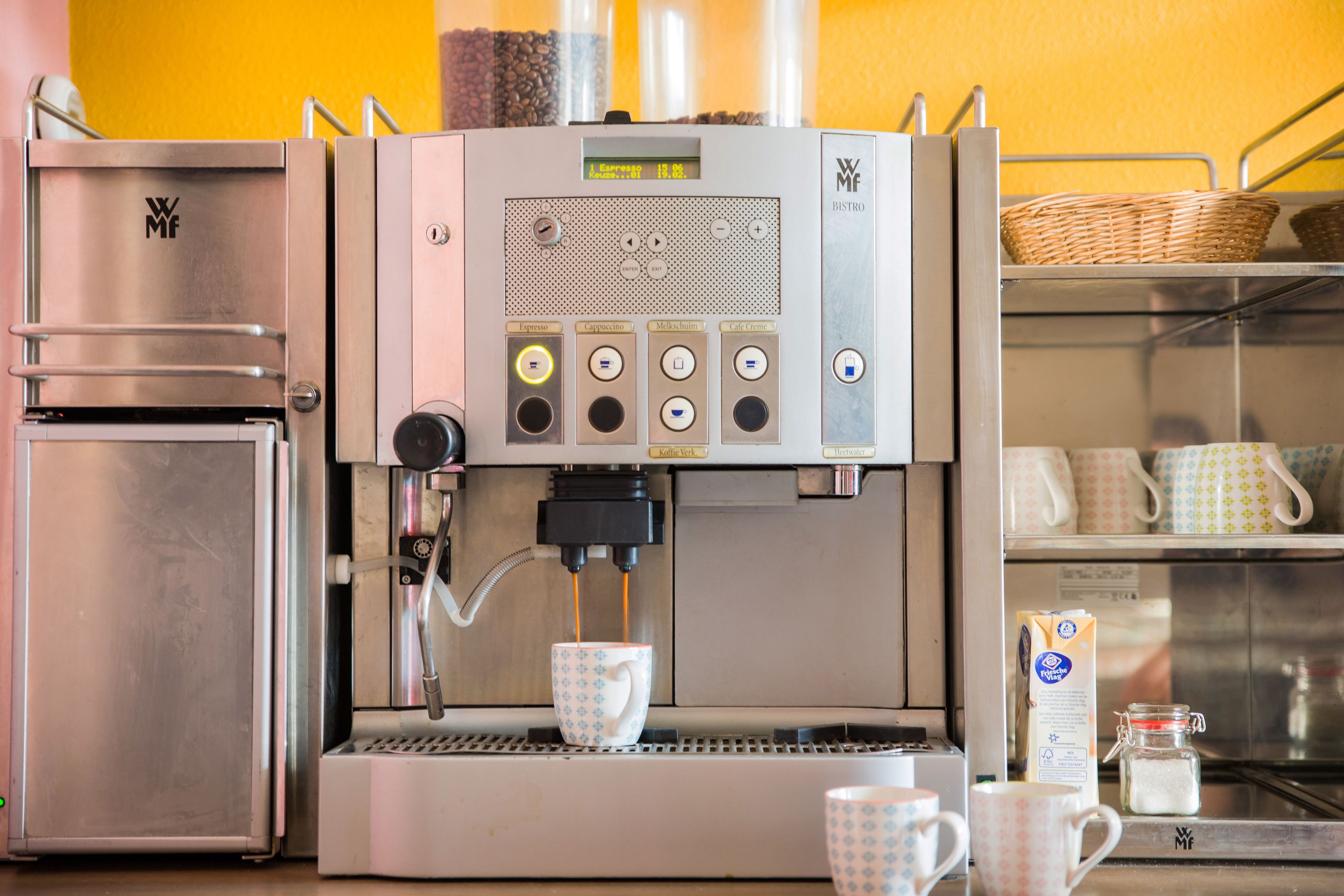 A coffee machine with a digital display, a milk frother, and a coffee cup.