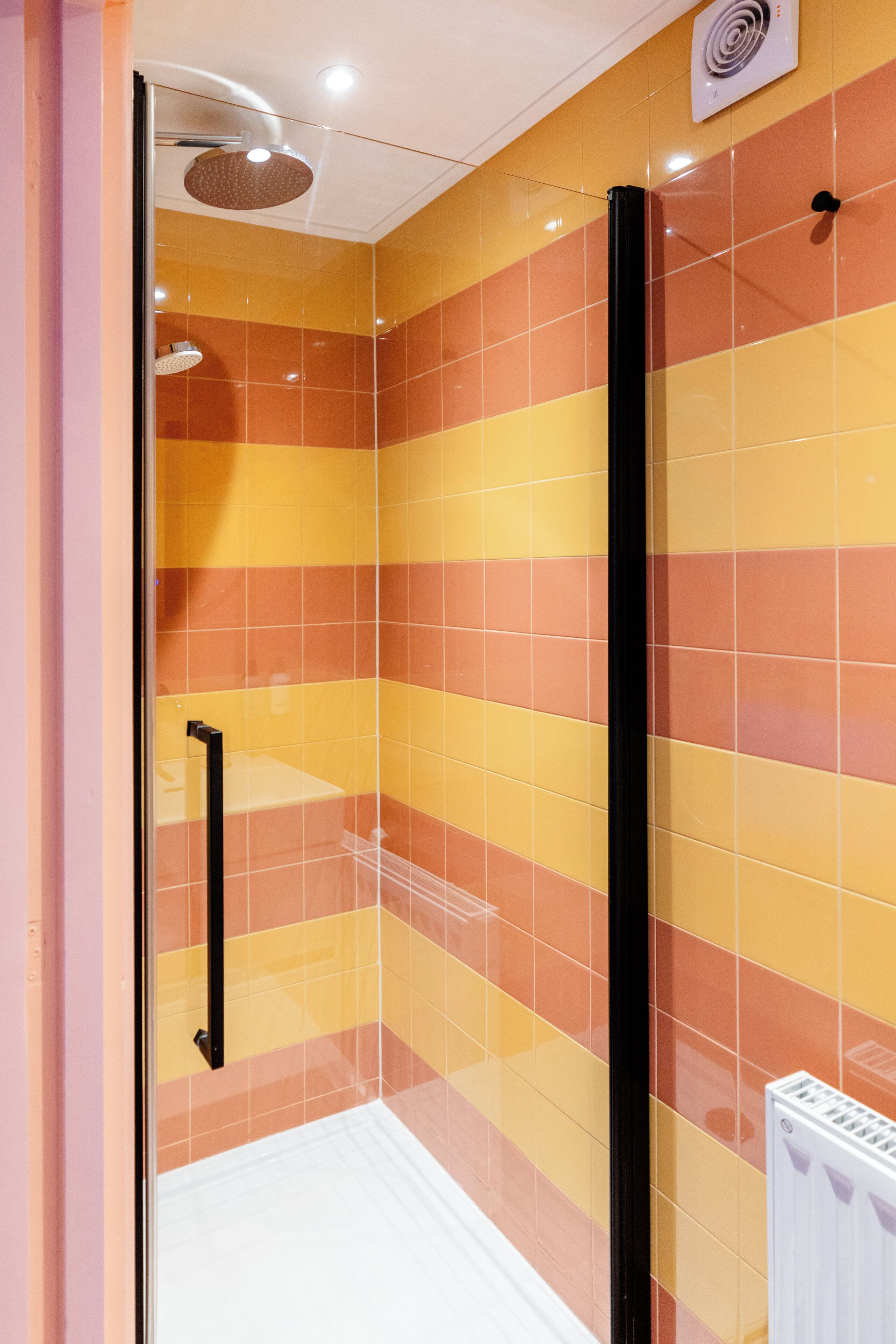 Un baño con puerta de cristal, ducha y radiador blanco.