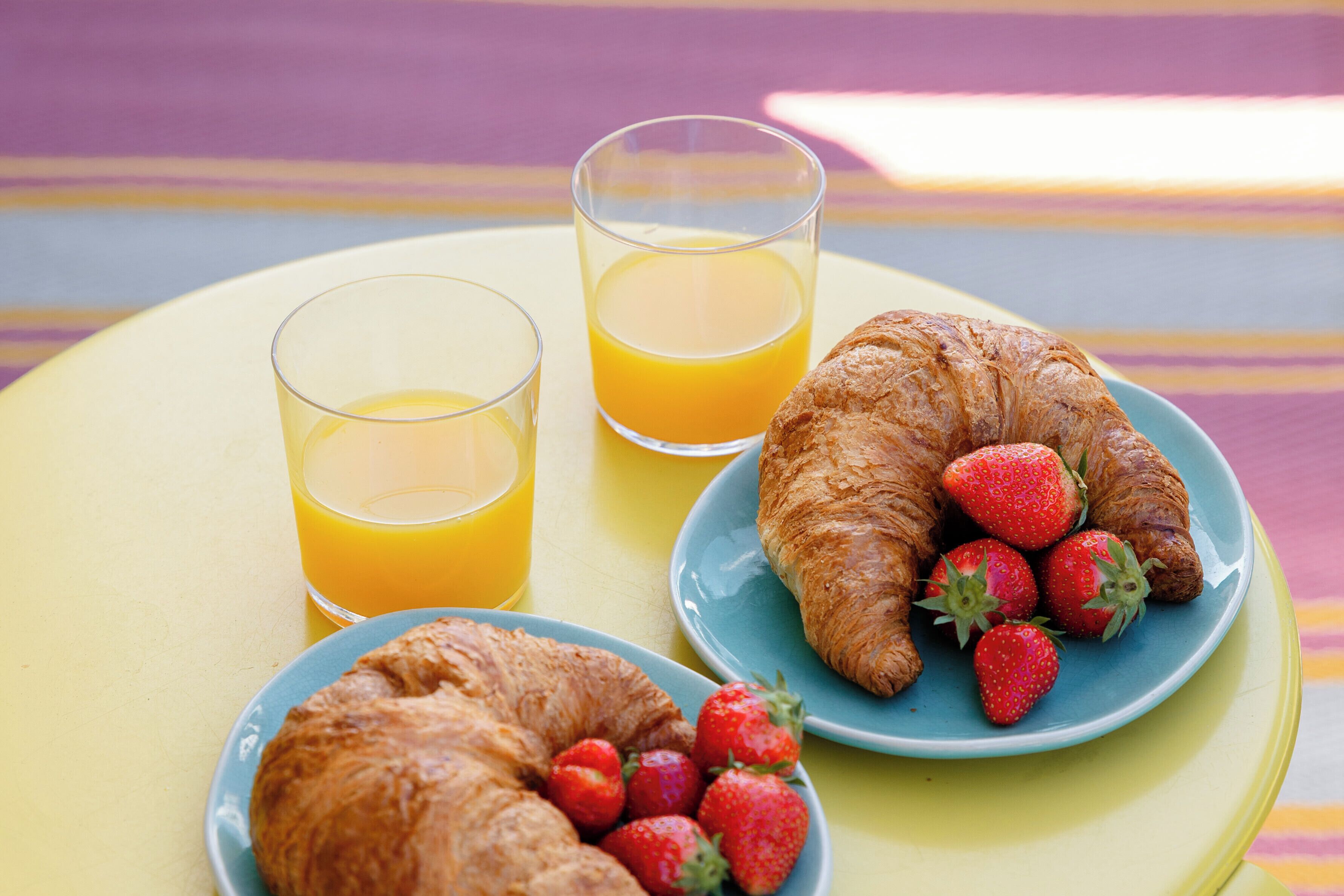 A table with two plates of food, one with croissants and strawberries, and two glasses of orange juice.