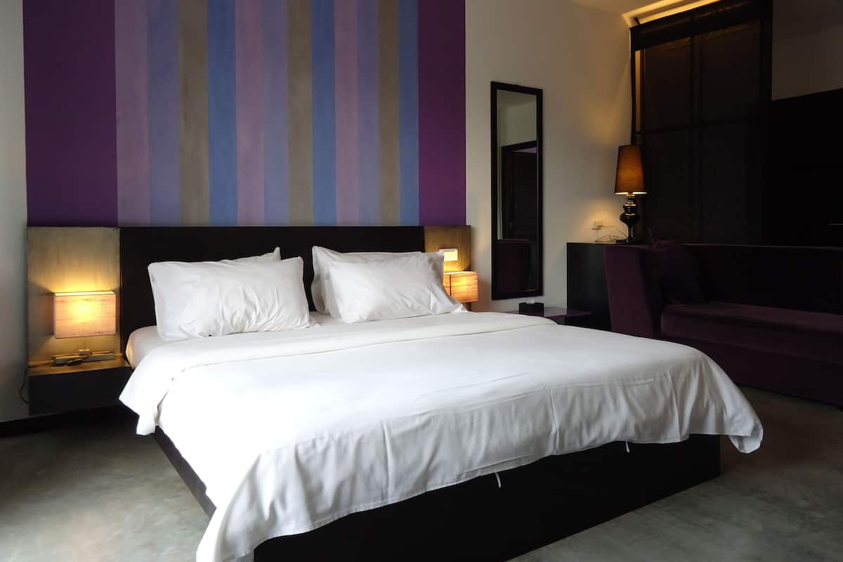A hotel room with a large bed, two bedside tables with lamps, a large mirror, and a purple armchair.