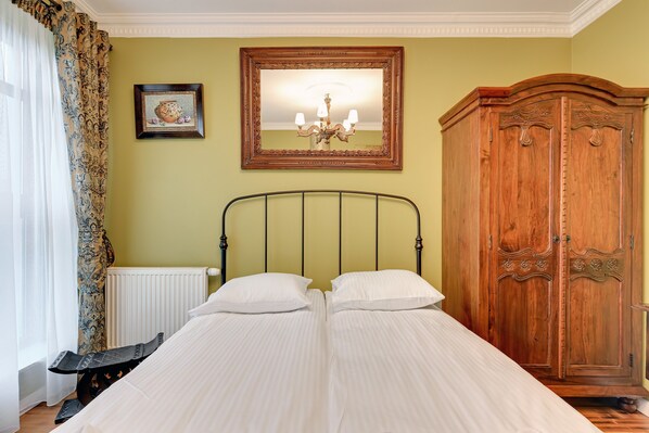 A room with a bed, a wooden wardrobe, a radiator, a framed picture, and a chandelier.