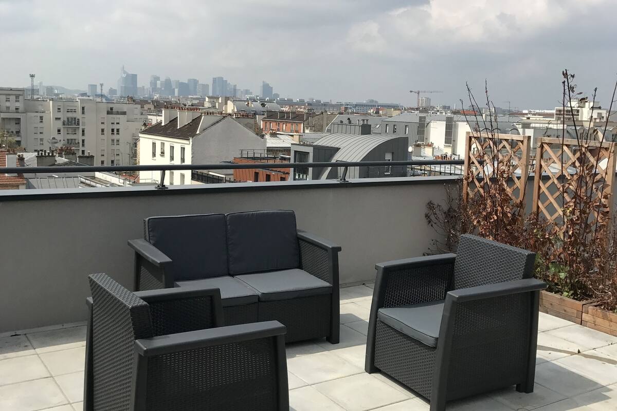 Une terrasse sur le toit, aménagée avec du mobilier d’extérieur, offrant une vue sur les toits de la ville et un ciel dégagé.