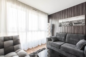 Una sala de estar con un sofá gris, un sillón gris y una obra de arte con un paisaje urbano en blanco y negro en la pared.