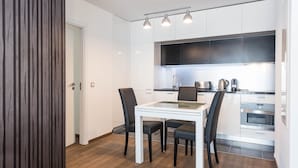 A modern kitchen with white cabinets, a black countertop, and a glass dining table with four chairs. - Les Appartements Paris Clichy (Clichy)