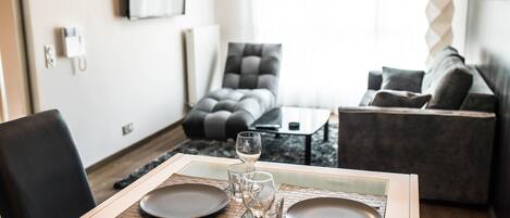 A dining area with a table set for two, a sofa, and a coffee table in a modern living space.