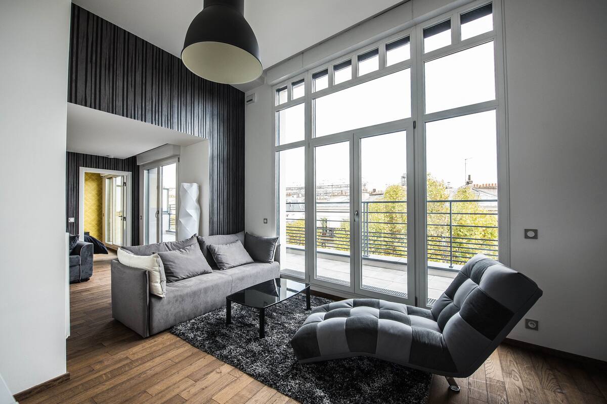 Un salon moderne doté d’une grande fenêtre, d’un canapé gris, d’un fauteuil noir et blanc et d’une table basse noire.