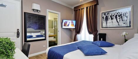 A hotel room with a bed, a TV, a bathroom, and a plant.