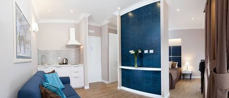 A modern living room with a blue sofa, a kitchen area with white cabinets, and a blue accent wall.