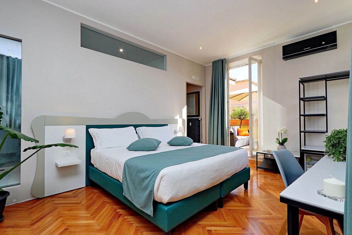 A modern hotel room with a bed, bedside table, and a small desk with a chair.