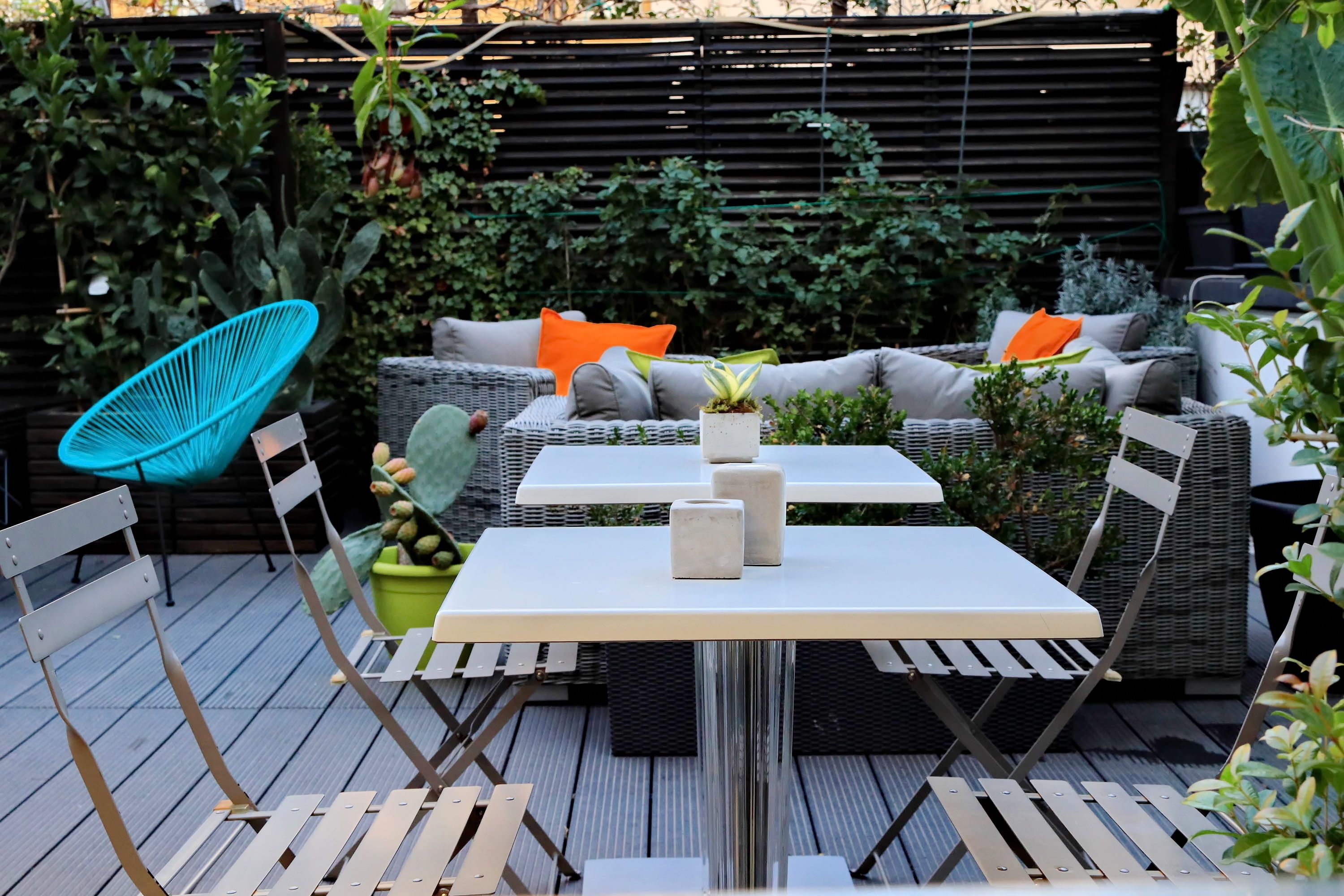 Een terras buiten met rieten meubels, een tafel en potplanten.