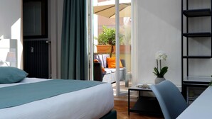 A hotel room with a bed, a desk, a chair, a potted plant, and a view of the outdoor seating area. - Vico Rooms and Terrace (Rome)
