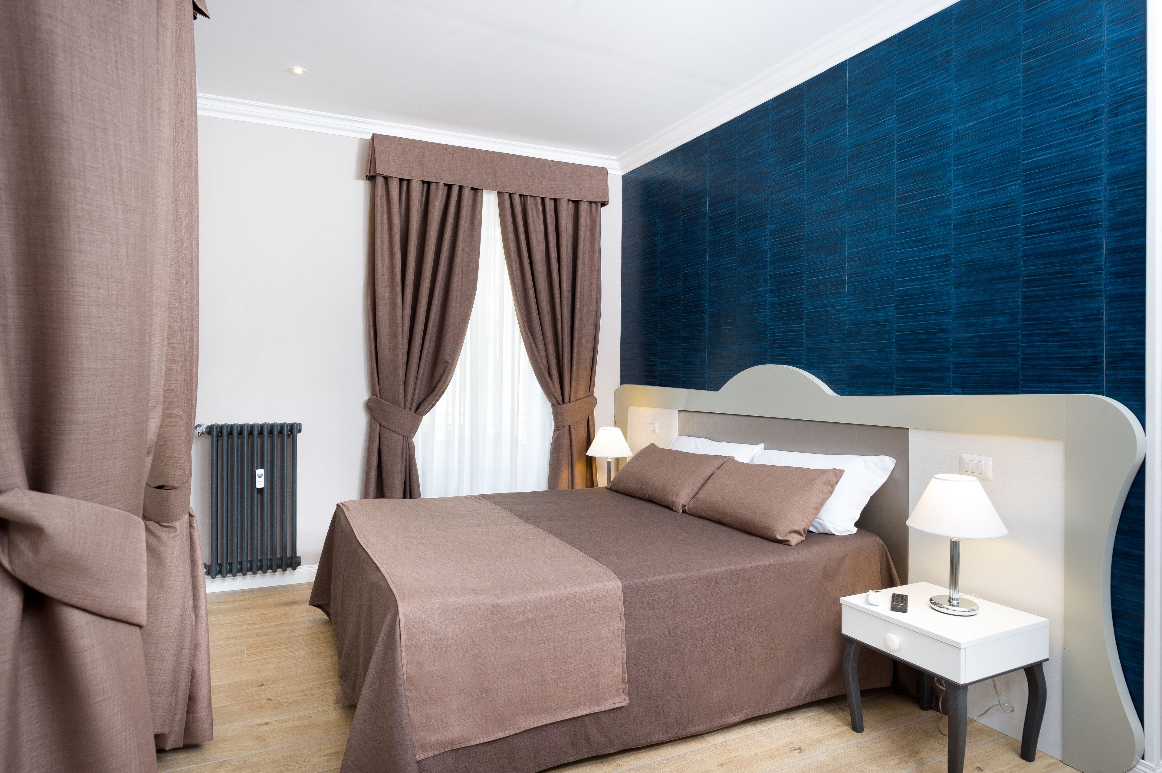 Un dormitorio con cama, mesita de noche, lámpara y cortinas.