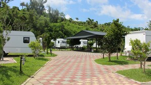 Un camping con vehículos recreativos, un área de picnic techada y un sendero pavimentado.