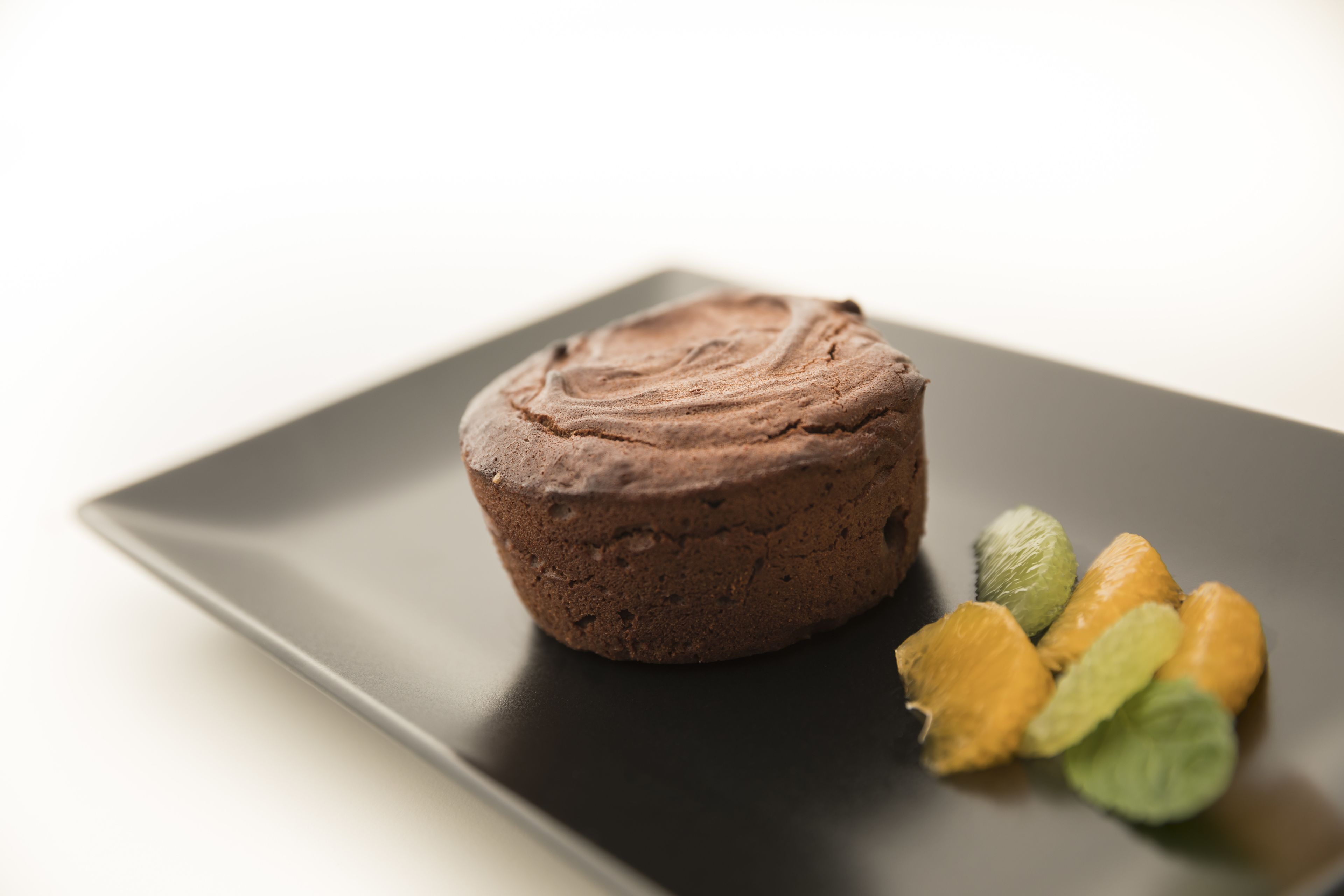 Sobremesa de chocolate num prato preto, com algumas frutas ao lado.