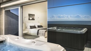 A modern spa area with a hot tub, a cozy bedroom with a bed and a painting, and a large window offering a view of the ocean.