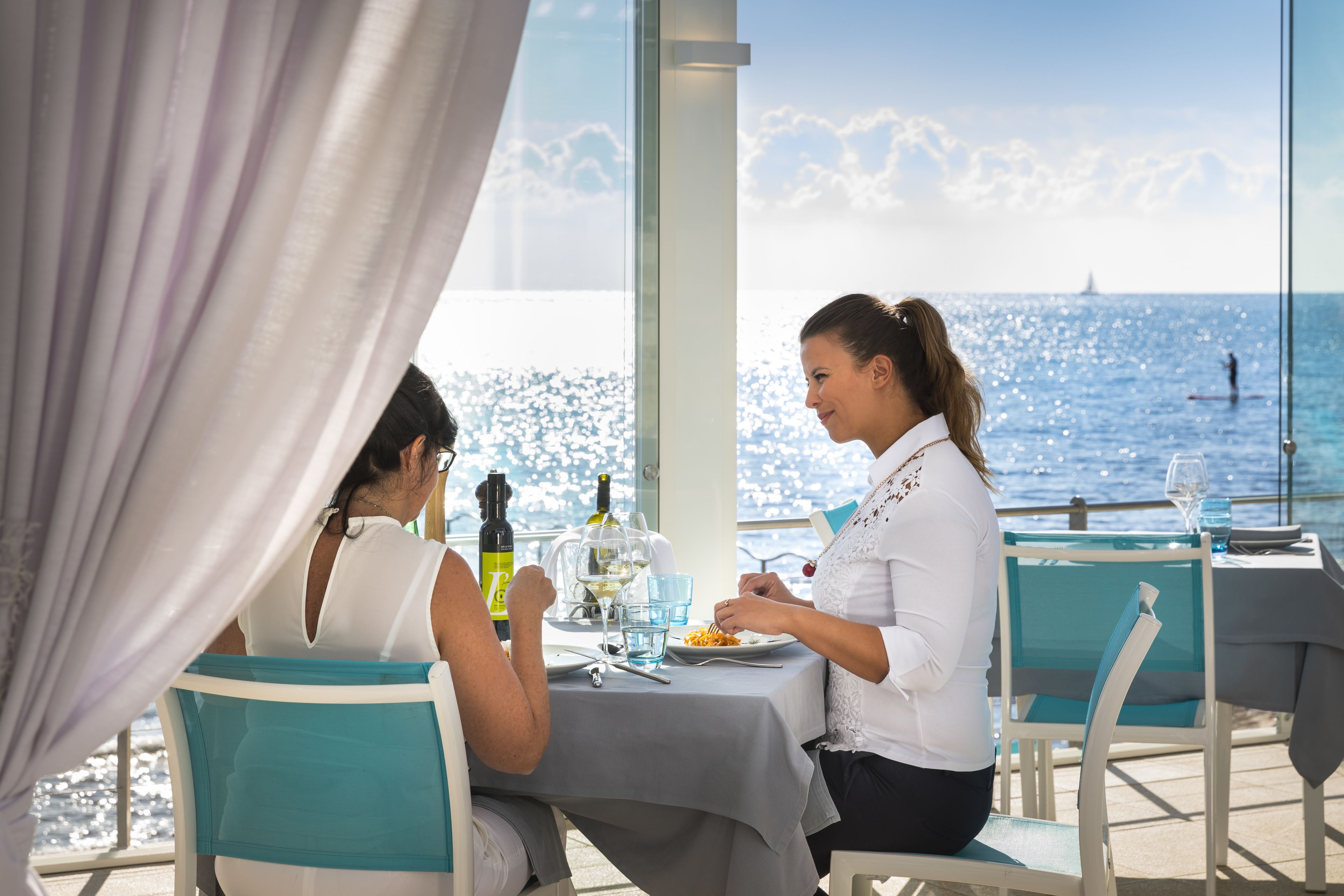 A dining table with a view of the sea, a bottle of wine, and a glass of water.