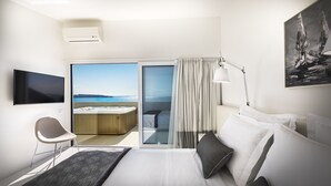 A modern hotel room with a bed, a chair, a desk, a TV, a painting, and a balcony with a view of the sea.