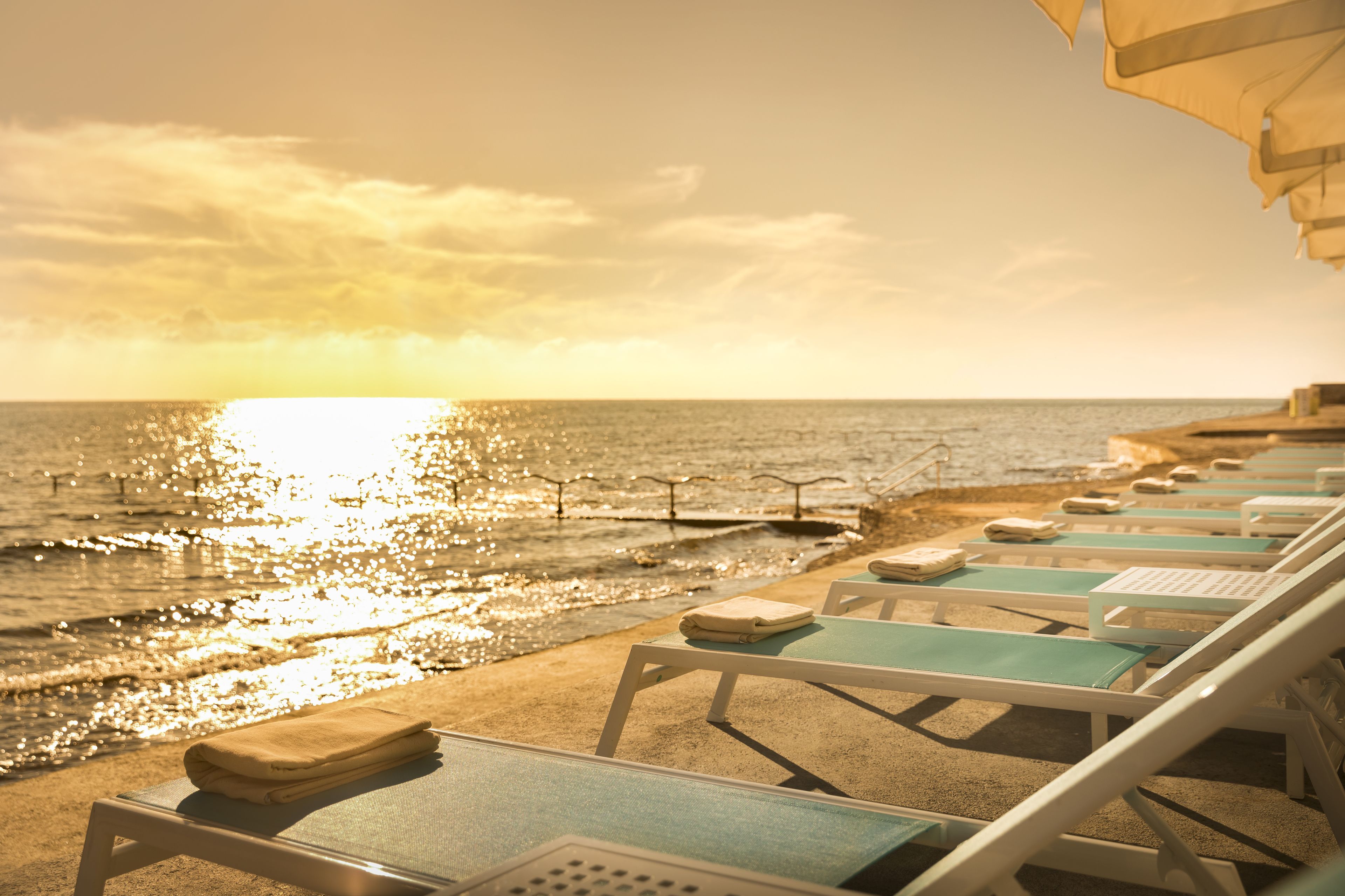 A beachside lounge area with sun loungers and a view of the ocean at sunset.
