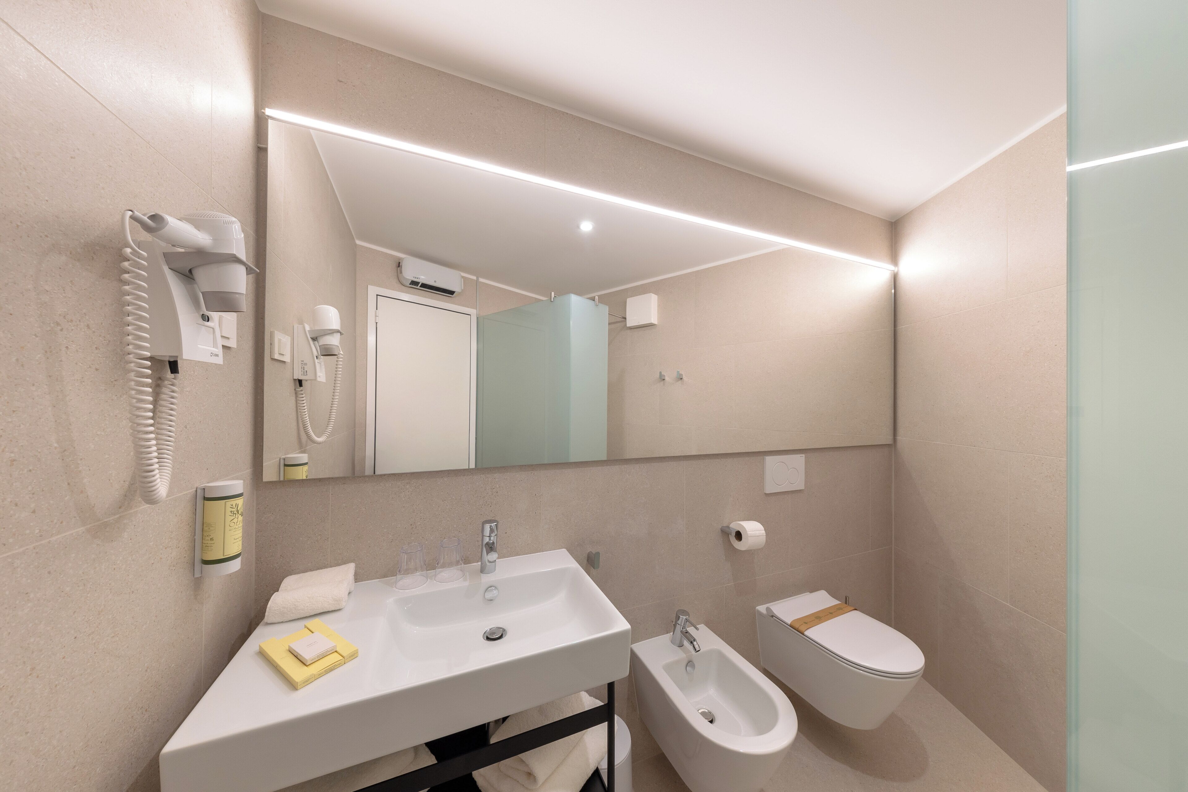 A modern bathroom with a large mirror, a sink, a bidet, and a hairdryer.