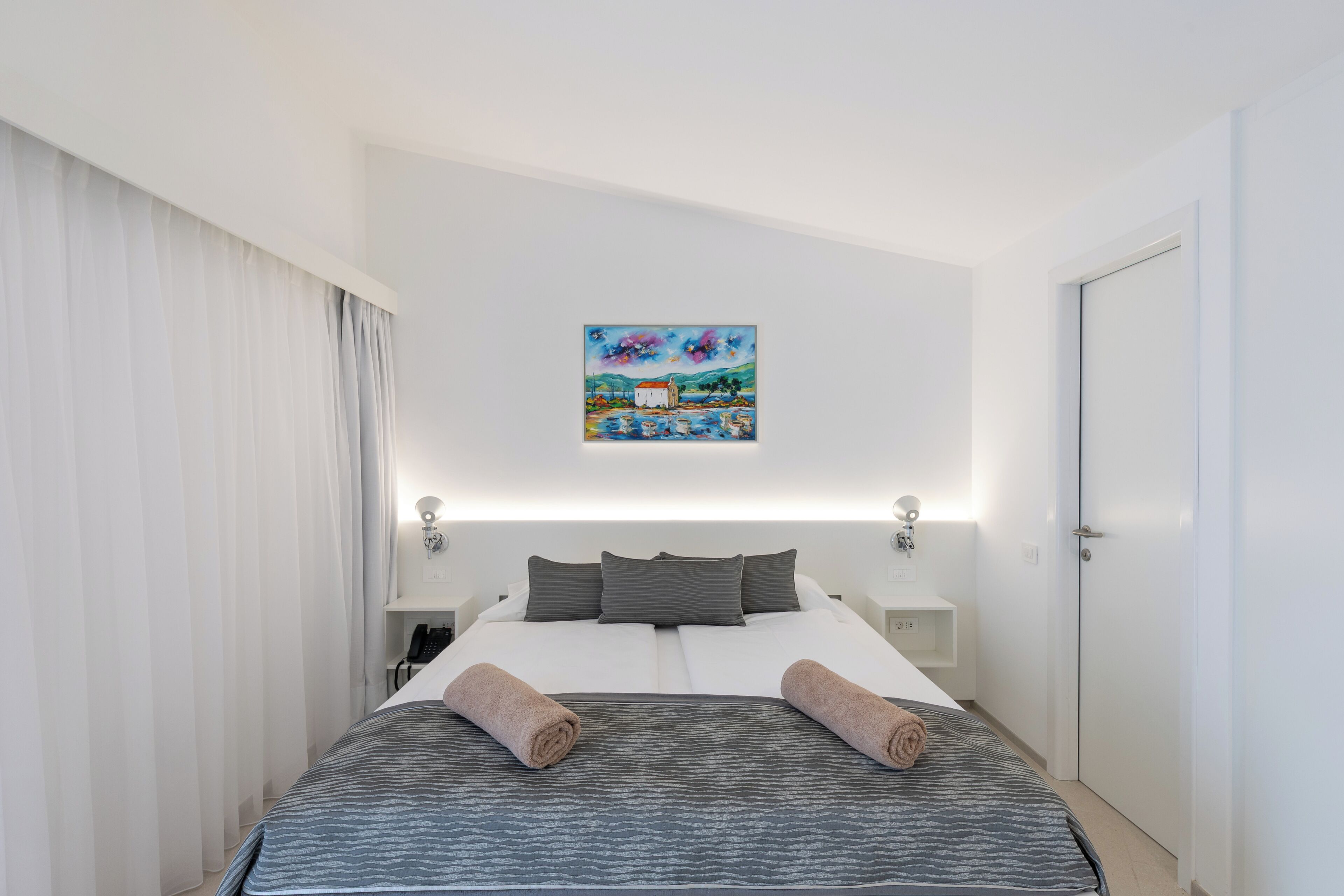 A hotel room with a bed, a painting, a telephone, and a door.
