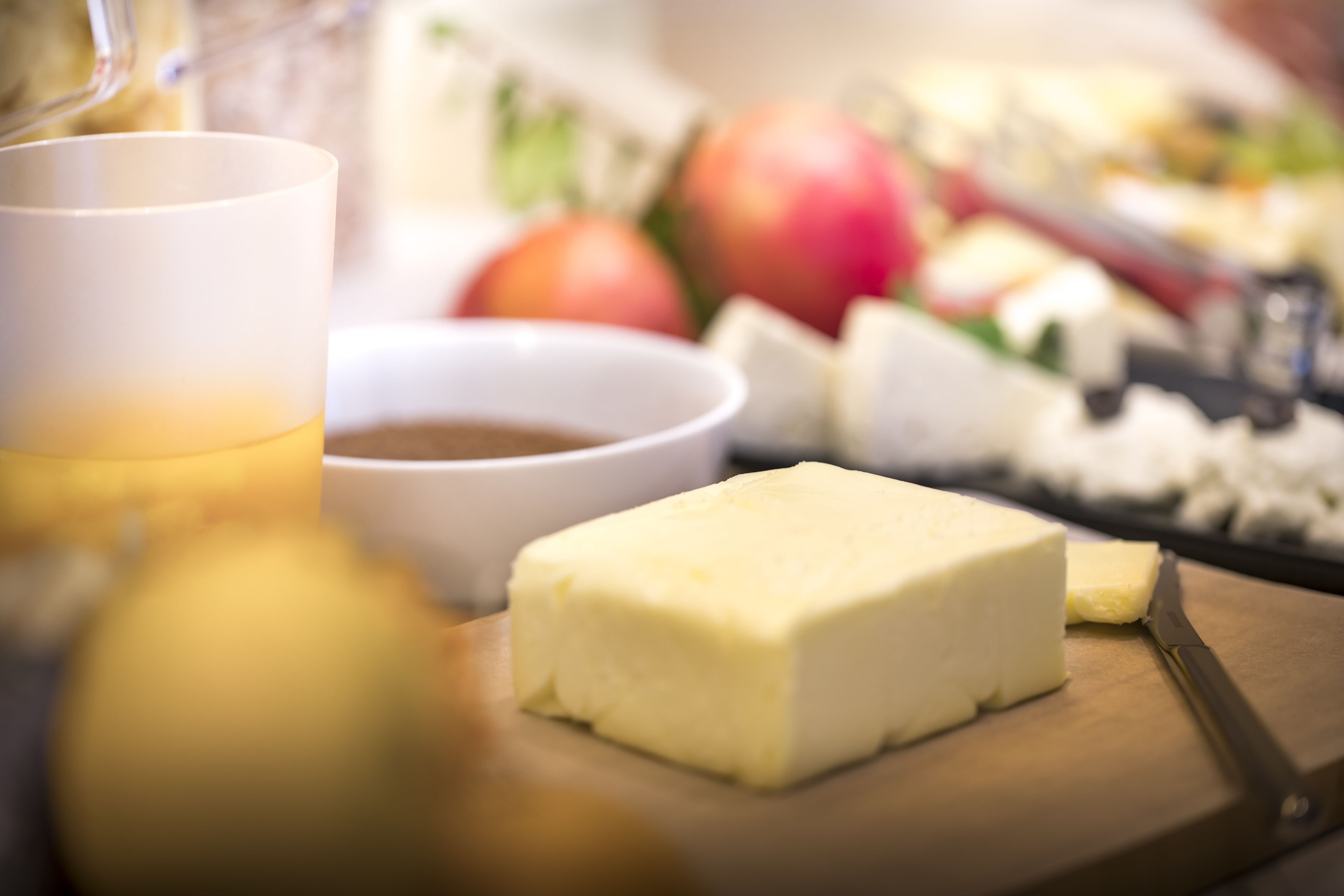 A cheese platter with a knife, a bowl of dip, and a glass of juice on a wooden board.