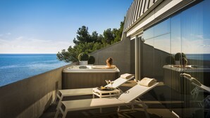 A balcony with a hot tub, lounge chairs, and a table with a plate of food and drinks.