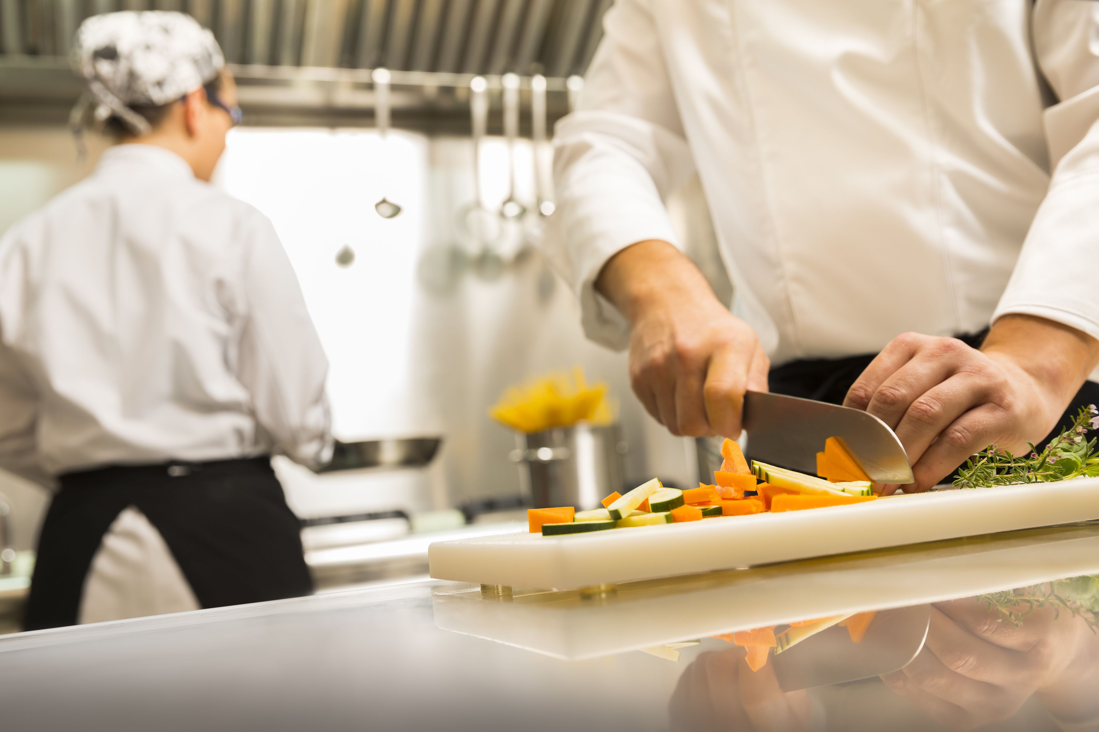 Un chef corta verduras sobre una tabla de cortar en una cocina.