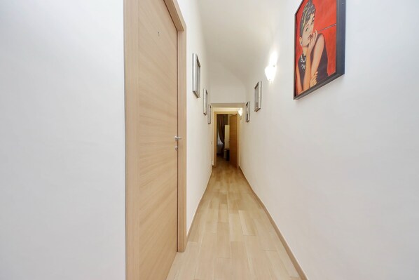 A narrow hallway with wooden flooring, white walls, and a framed picture on the right. - Dream City Rome (Rome)