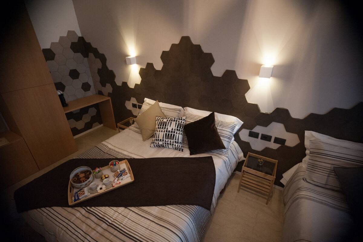 A neatly made bed with a tray of breakfast items, a bedside table, and a wall with a geometric pattern.