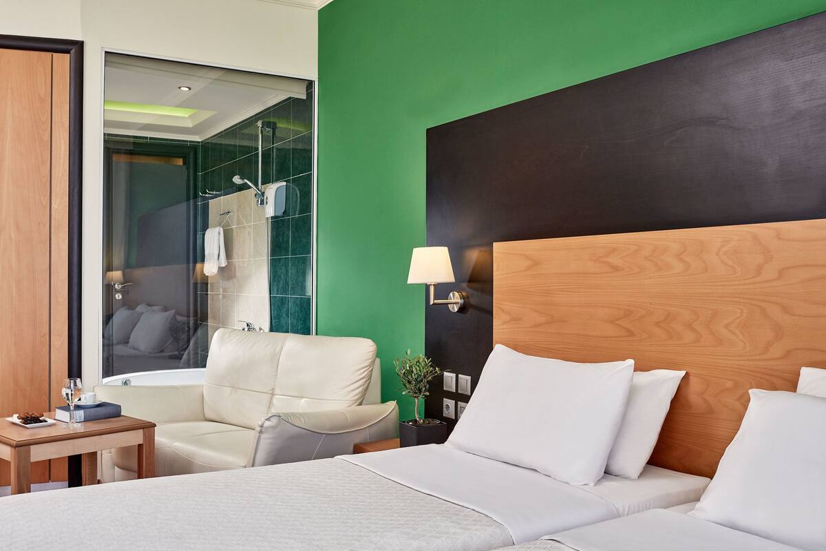 Una habitación de hotel con una cama, una silla, una mesita con un vaso de agua y una mesita de noche con una lámpara.