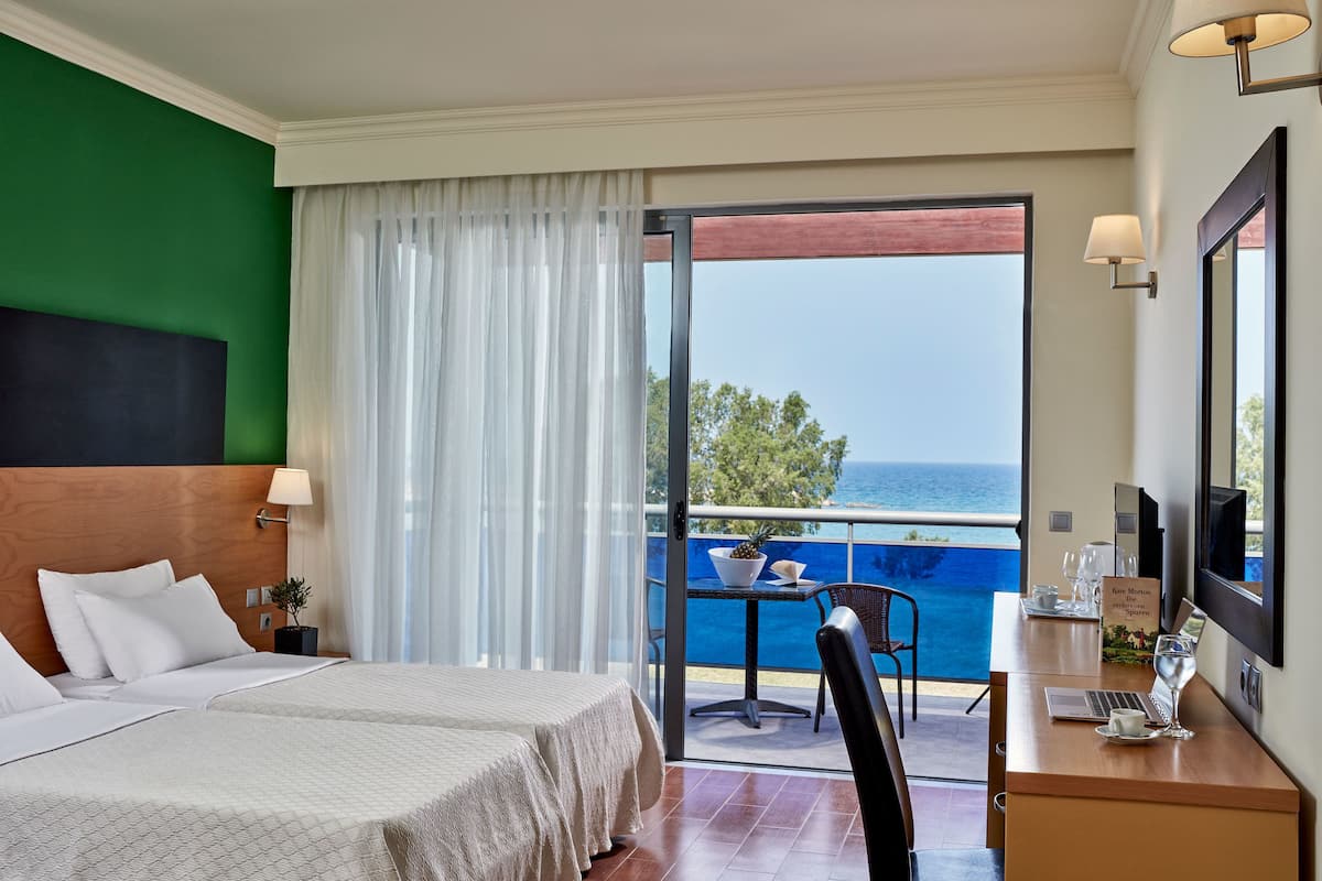 Una habitación de hotel con una cama, un escritorio con una computadora portátil, una silla y vista al océano.