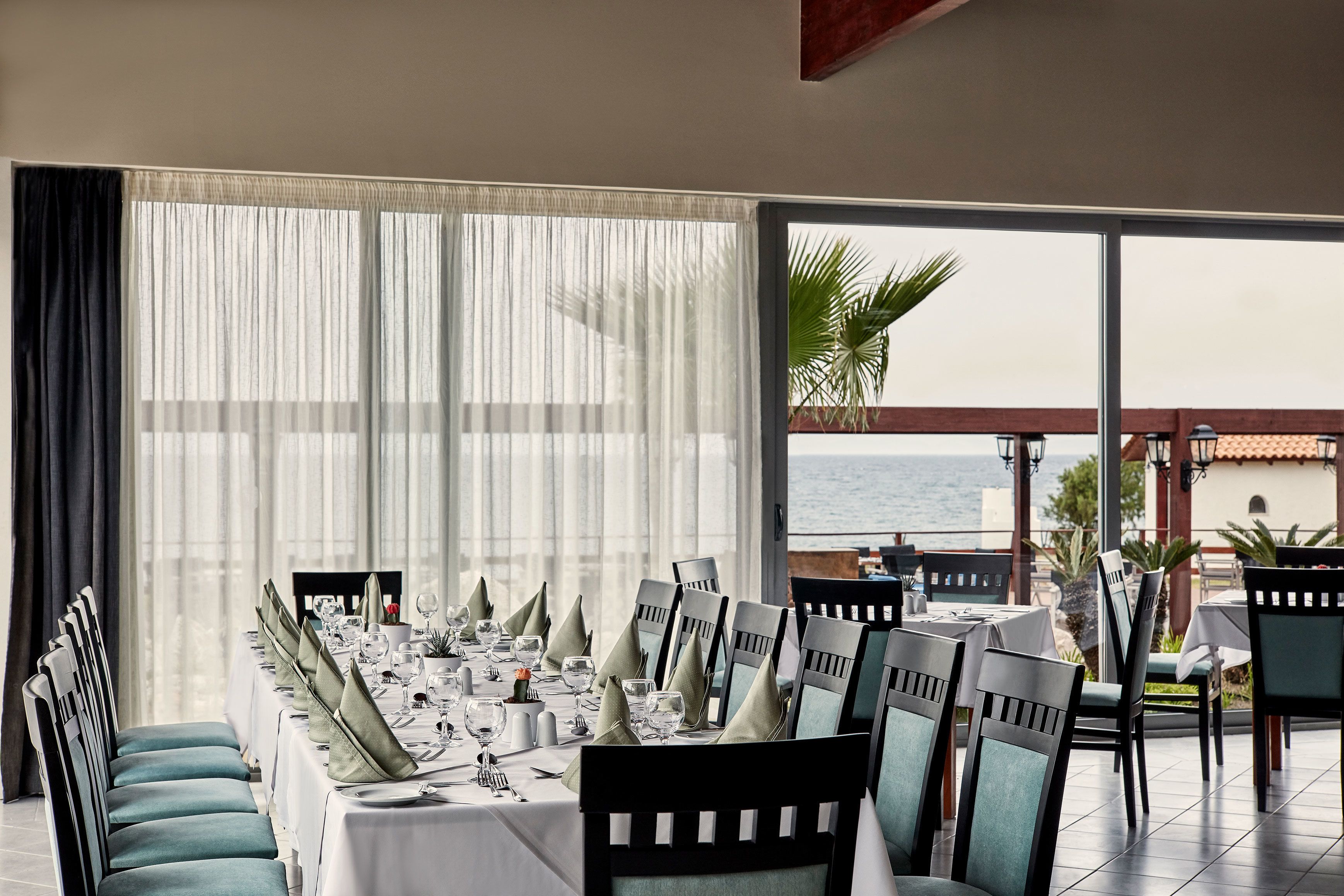 A dining area with a table set for a meal, chairs, and a view of the sea through large windows.