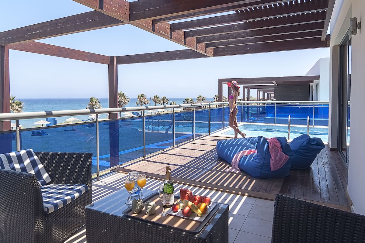 Un balcón con mobiliario de mimbre, una mesa con bebidas y frutas, y vista al océano.
