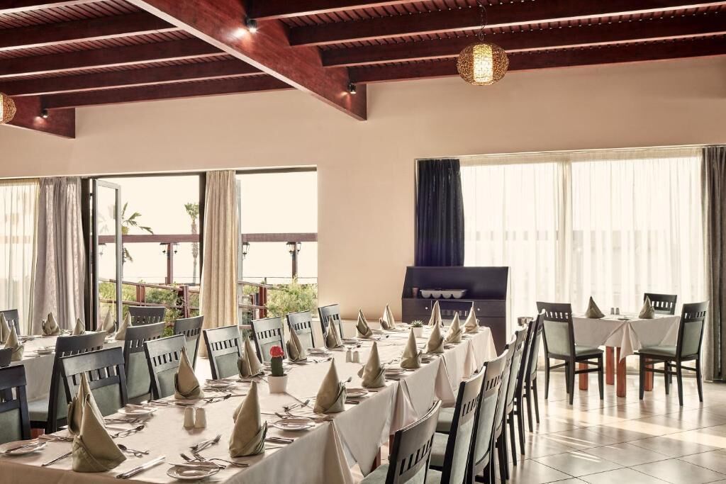 Un comedor con mesas dispuestas para una comida, ventanas amplias y vistas al exterior.