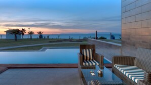 A poolside area with wicker furniture, a view of the sea, and a modern building facade.