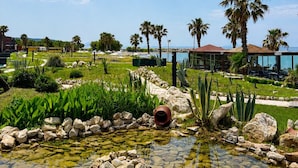 Un jardín ajardinado con un estanque, palmeras y un edificio con amplios ventanales.