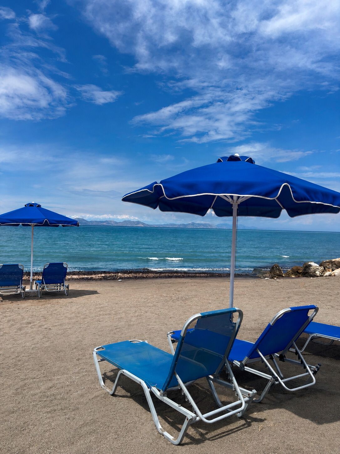 A beach with blue umbrellas and lounge chairs.