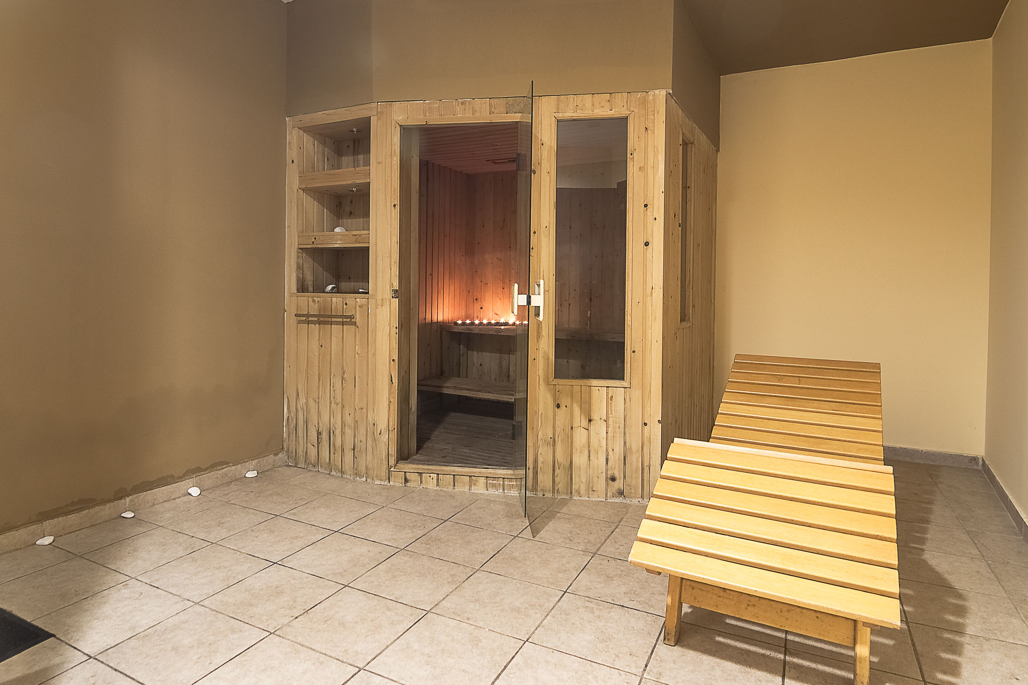 Eine Holzsauna mit Sitzbank, Fliesenboden und offenem Feuer.