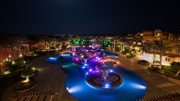 Un complexe hôtelier ouvert la nuit, doté d’une piscine, de palmiers et de chemins éclairés.