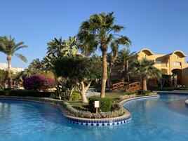A swimming pool with a curved edge, surrounded by palm trees and a wooden bridge.