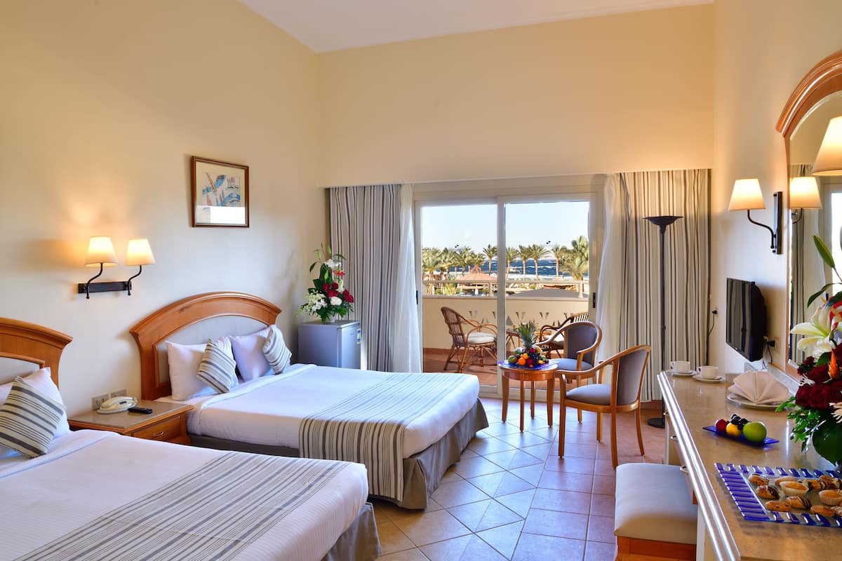 A hotel room with two beds, a dining area with a table and chairs, a balcony with a view, and a TV.