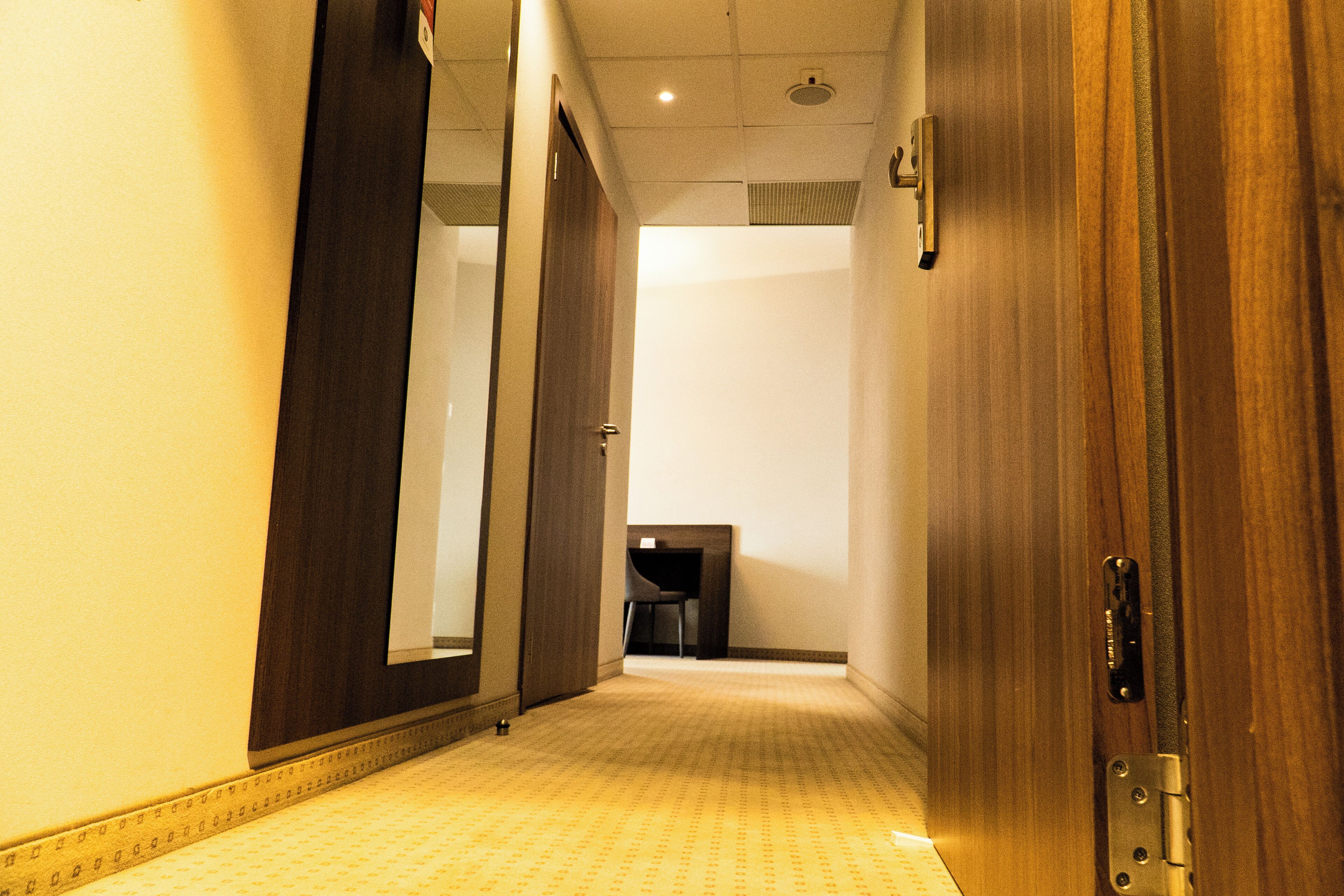 Pasillo de hotel con puertas de madera, suelo alfombrado y un escritorio pequeño con una silla a lo lejos.