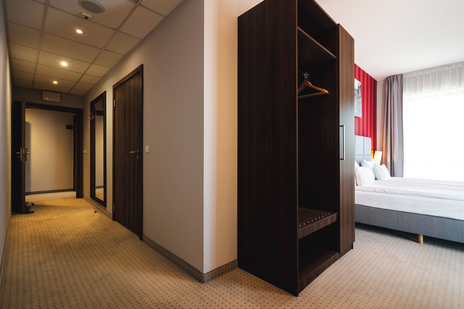 A hotel room with a bed, a wardrobe, a mirror, and a hallway.