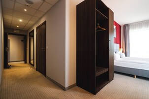 A hotel room with a bed, a wardrobe, a mirror, and a hallway.