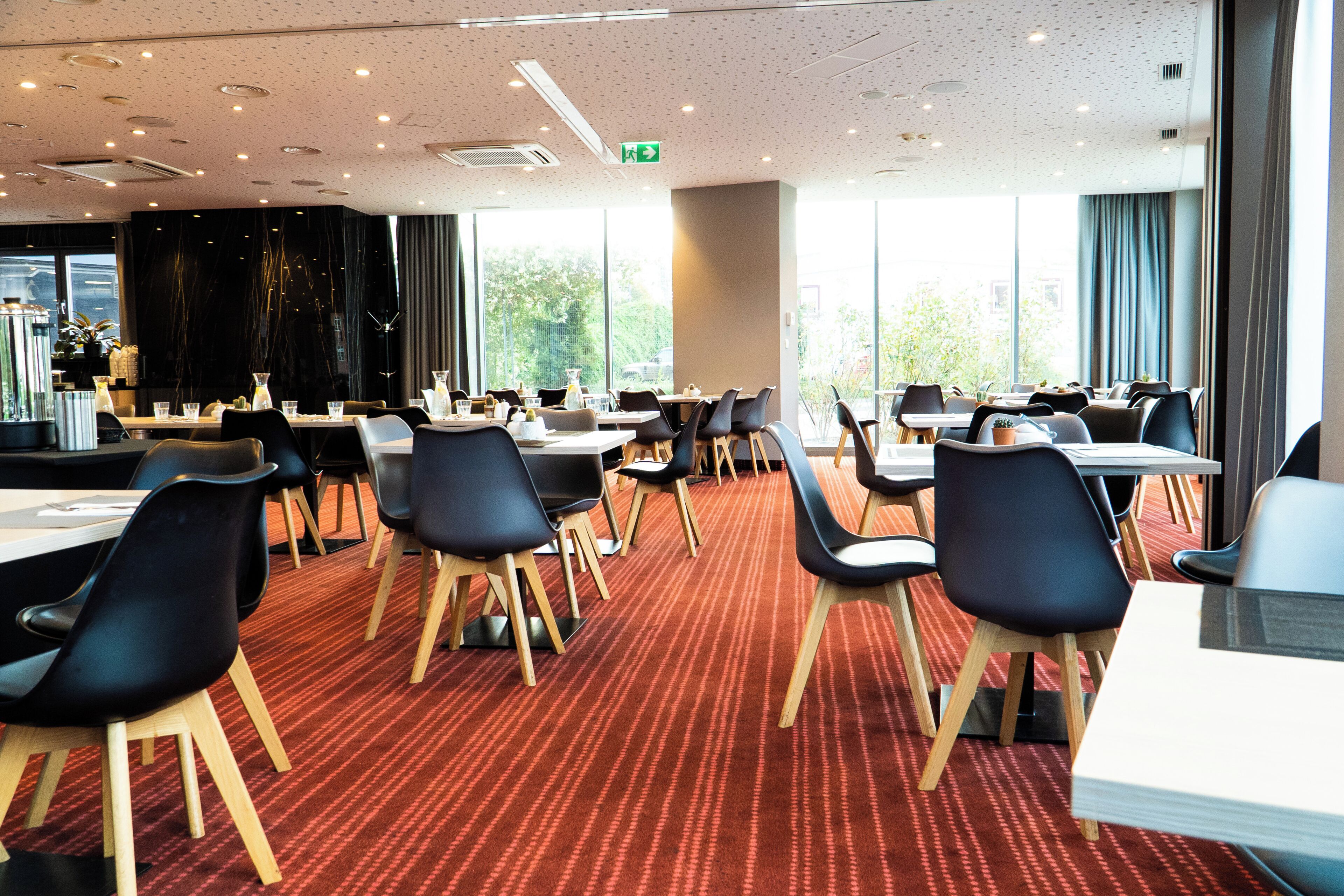A modern dining area with tables and chairs, large windows, and a red carpeted floor.