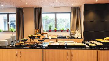 A buffet setup with various food items and a view of greenery outside.