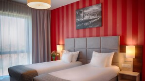 Een hotelkamer met twee bedden, een stadslandschap op de muur en uitzicht op de stad door dunne gordijnen.